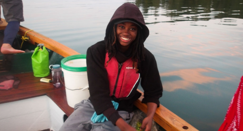 A person wearing a lifejacket smiles while sitting in a boat on calm water
